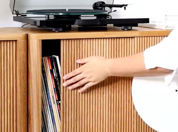 Een hand schuift een houten Cloe-deur met structuur onder een platenspeler
