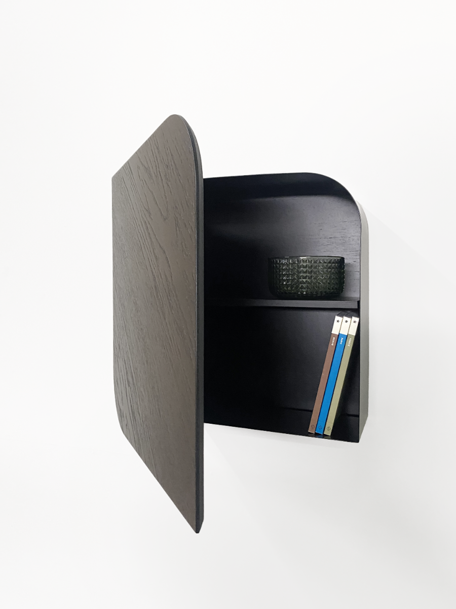 Small black storage unit with a door open, revealing books and a basket inside on a white background