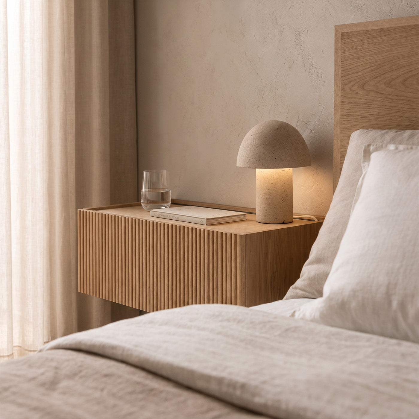 Dalea floating bedside table in oak with a grooved drawer and raised top beside a bed